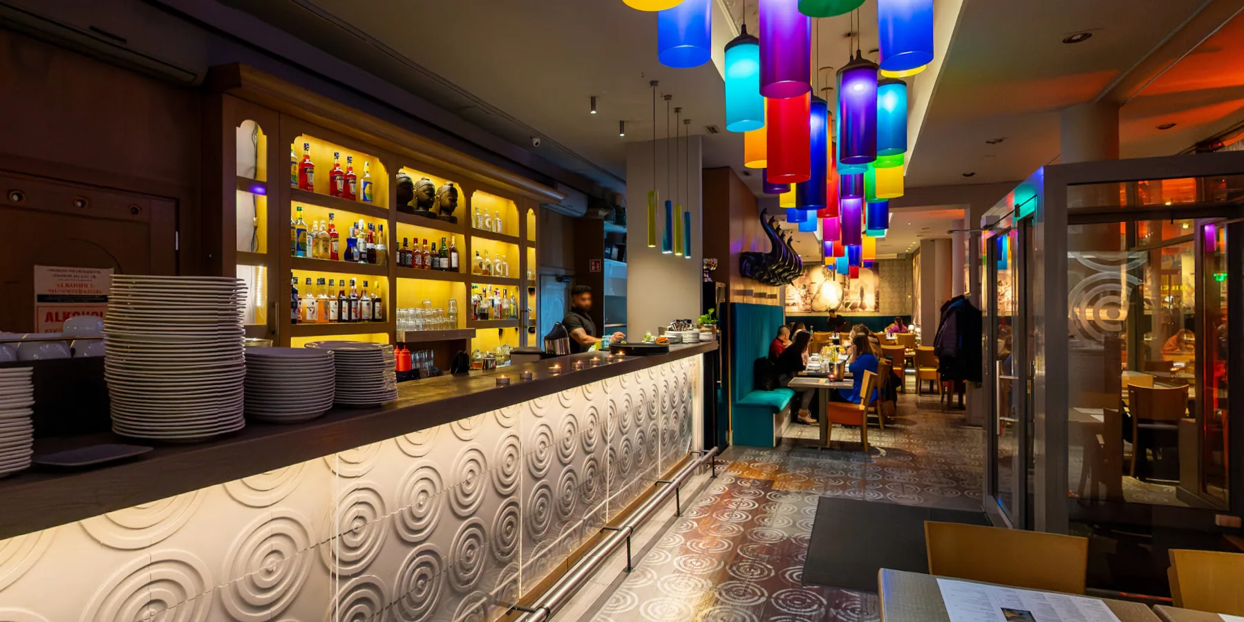 Wnętrze restauracji Masala we Wrocławiu: bar z podświetlanymi półkami, kolorowe lampy nad przejściem i sala z gośćmi. Kadr ze spaceru 360°.